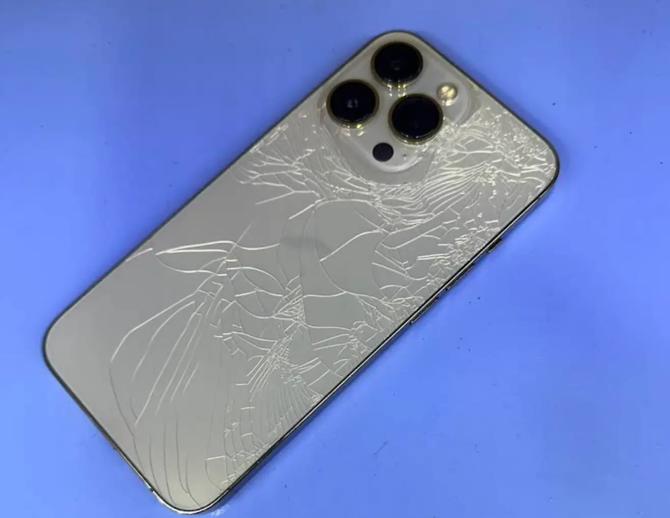 Cracked iPhone back glass with visible damage to the camera area and surrounding panel